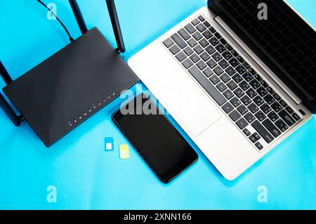 Router Wi-Fi, scheda SIM, smartphone, computer portatile su sfondo blu. Apparecchiature di comunicazione Foto Stock