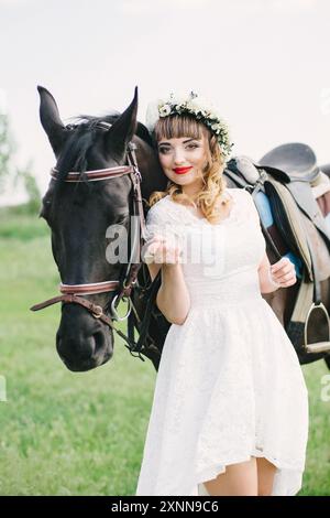 ragazza con labbra rosse in un abito bianco vicino a un cavallo nero Foto Stock