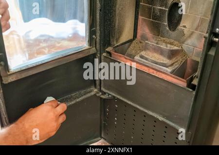 Primo piano di un uomo che pulisce la fuliggine prodotta dalla stufa a pellet nel suo soggiorno, calore sostenibile. Energia rinnovabile. Foto Stock