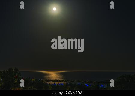 Calmo scenario di spiaggia di notte con il chiaro di luna che si riflette sul Mar Mediterraneo, creando un percorso luminoso sulla superficie dell'acqua. Grecia. Foto Stock