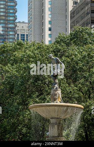 New York, New York, Stati Uniti - 2 agosto 2023: Fontana Pulitzer sul primo piano di Pulitzer Plaza, fogliame verde sul retro con facciate di grattacieli sopra Foto Stock