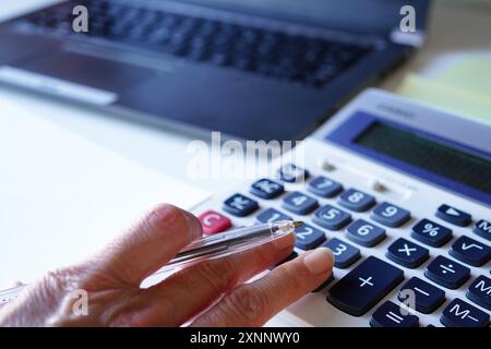 La mano di una consulente donna anziana che fa calcoli su una calcolatrice nel suo ufficio Foto Stock