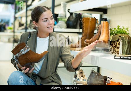 L'acquirente femminile guarda le calzature della nuova collezione e acquista un nuovo paio di stivali per l'inverno. Foto Stock