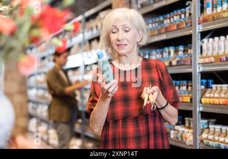 La donna anziana sceglie pigmenti multicolore per i suoi futuri piatti in argilla o ceramica in un negozio specializzato Foto Stock