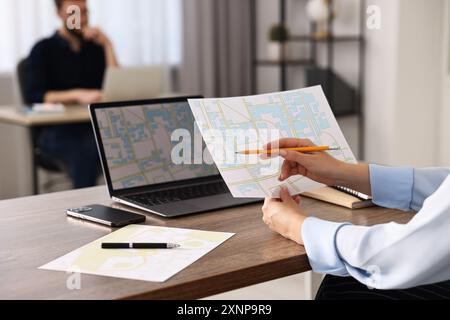 Cartografo che lavora con mappe catastali al tavolo di legno in ufficio, primo piano Foto Stock