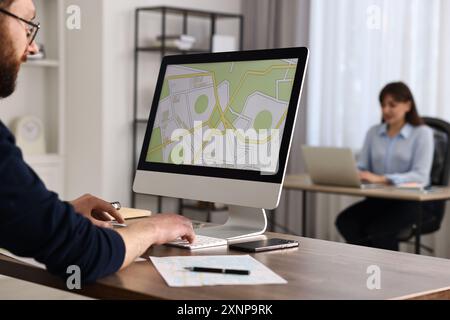 Cartografo che lavora con una mappa catastale al computer al tavolo di legno in ufficio, primo piano Foto Stock