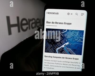 Persona che detiene un cellulare con la pagina web della società tecnologica tedesca Heraeus Holding GmbH davanti al logo. Concentrarsi sul display del telefono centero f. Foto Stock