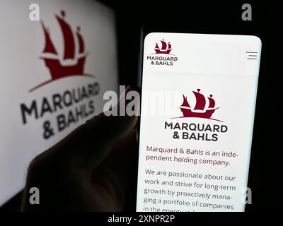 Persona che detiene un cellulare con pagina web della società energetica tedesca Marquard e Bahls AG davanti al logo aziendale. Messa a fuoco al centro del display del telefono. Foto Stock