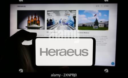 Persona che detiene un cellulare con il logo della società tedesca di tecnologia Heraeus Holding GmbH di fronte alla pagina web aziendale. Mettere a fuoco il display del telefono. Foto Stock