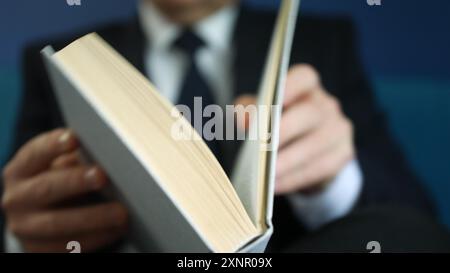 Uomo d'affari in tuta che legge un libro stando in piedi su sfondo blu. Spazio per il testo. Concetto di educazione e lettura di libri Foto Stock