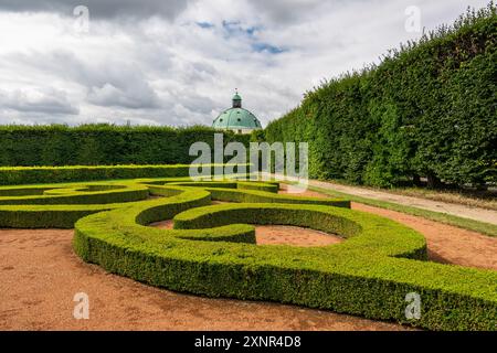 Vista bassa del giardino ornamentale di fiori con cespugli verdi, giorno di sole estivo, edificio storico rotondo nel centro, turismo nella Repubblica Ceca Foto Stock