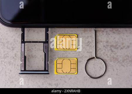 Smartphone e slot aperti per schede micro SD e nano SIM, due schede nano SIM e chiave in metallo su sfondo grigio vista dall'alto Foto Stock