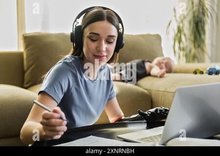 Una giovane donna con protesi e cuffie sembra un libro da lavoro e un notebook Foto Stock