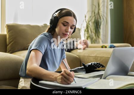 Una giovane donna con protesi e cuffie sembra un libro da lavoro e un notebook Foto Stock