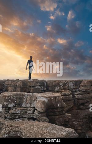 Persona in piedi su Rugged Cliff al tramonto con il cielo drammatico in Portogallo Foto Stock