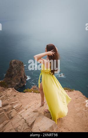 Donna in abito giallo sulla scogliera Rocky con vista sull'Oceano Atlantico in Portogallo Foto Stock