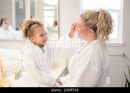 La bambina sta spazzolando il trucco sulle madri in bagno Foto Stock