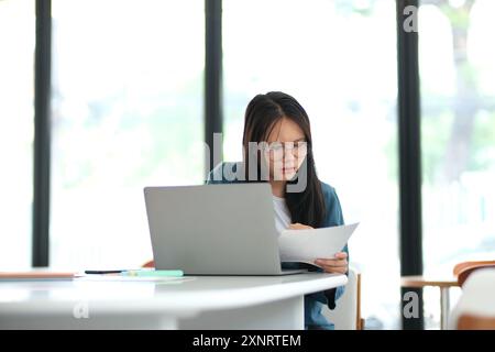 Una donna è seduta a una scrivania con un portatile e un pezzo di carta Foto Stock