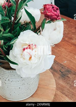 Peonie bianche e rosa in un vaso di ceramica su una superficie di legno. Foto Stock