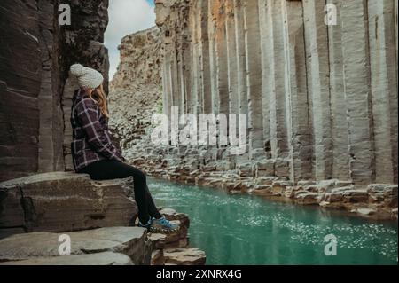 Donna seduta su colonne di basalto nel canyon di Stuðlagil, Islanda Foto Stock