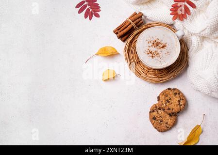 Composizione accogliente autunnale. Tazza di caffè cappuccino, plaid lavorato a maglia, biscotti con scaglie di cioccolato e foglie autunnali gialle su sfondo bianco, vista dall'alto, copia Foto Stock
