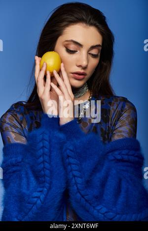 Una giovane donna con un maglione blu tiene un limone contro la guancia. Foto Stock