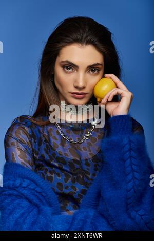 Una giovane donna con una camicia blu e nera con stampa animale tiene un limone sul viso. Foto Stock