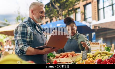 Agricoltori locali che gestiscono un'azienda a conduzione familiare, che offre prodotti agricoli sostenibili in vendita. Ritratto di un maschio di mezza età che utilizza un computer portatile per gestire l'inventario e gli ordini online di prodotti biologici Foto Stock