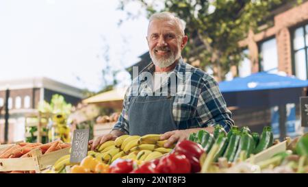 Ritratto di un uomo che gestisce uno stand di vendita di cibo di strada con prodotti agricoli naturali freschi. Happy Old Handsome Farmer con capelli e barba grigi guarda la fotocamera e sorride incredibilmente Foto Stock