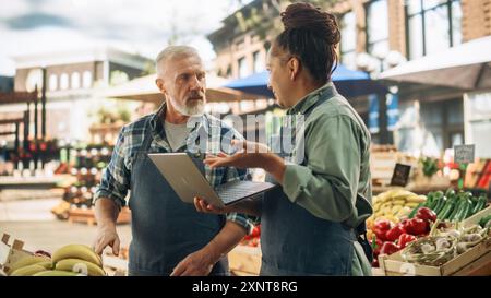 Partner commerciali di sesso femminile e maschile Gestione di un mercato di successo per agricoltori biologici. Coppia di adulti multietnici che parla dell'inventario dei prodotti agricoli durante l'utilizzo di un computer portatile Foto Stock