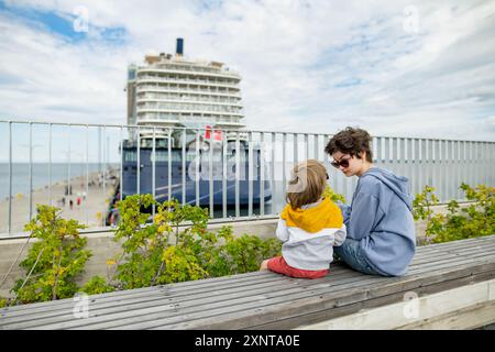 Il bambino carino e la sorella adolescente seduti su una panchina a guardare le navi da crociera attraccate nel porto di Tallinn. Foto Stock