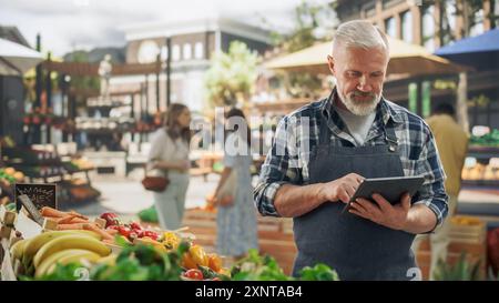 Ritratto di un agricoltore adulto che utilizza un tablet al lavoro mentre vende prodotti agricoli biologici freschi da una situazione di mercato. Uomo di mezza età che gestisce gli ordini online su un sito Web di e-commerce Foto Stock