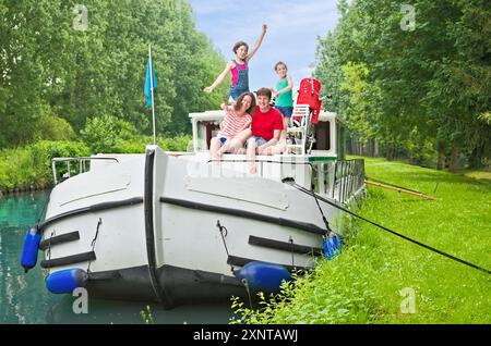 Vacanze in famiglia, vacanze estive in barca sul canale, bambini felici e genitori che si divertono con una crociera sul fiume in casa galleggiante in Francia Foto Stock