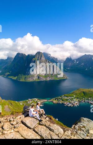 Due escursionisti godono della vista mozzafiato di un fiordo circondato da montagne sotto un cielo azzurro. Reinebringen Lofoten Norvegia Foto Stock
