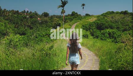 Una giovane donna si sta godendo la passeggiata sul crinale di campuhan vicino a ubud a bali, indonesia. E' circondata da una lussureggiante vegetazione verde e il sole splende Foto Stock