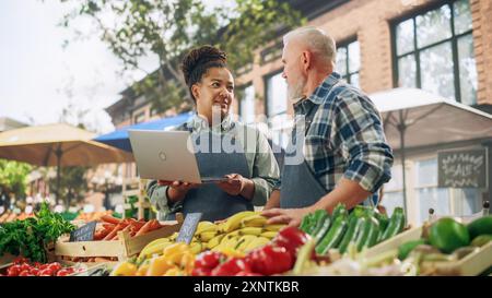 Partner commerciali di sesso femminile e maschile Gestione di un mercato di successo per agricoltori biologici. Coppia di adulti multietnici che parla dell'inventario dei prodotti agricoli durante l'utilizzo di un computer portatile Foto Stock