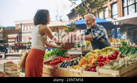 Cheerful Street Vendor gestisce una piccola azienda agricola, vendendo frutta e verdura sostenibili. Uomo di mezza età felice che riempie un sacchetto della spesa di carta riciclata con cibo naturale locale Foto Stock