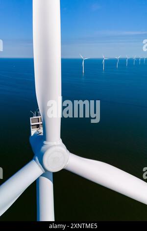 Le turbine eoliche si ergono alte nelle acque olandesi e sfruttano la potenza del vento per produrre energia pulita, mentre l'orizzonte si estende all'infinito attraverso un cielo blu vibrante. Foto Stock