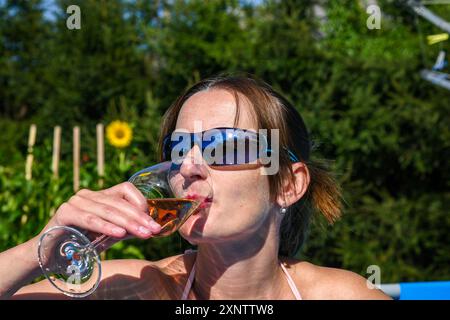 Una donna si sta godendo un bicchiere di vino in piscina in una giornata di sole. Foto Stock