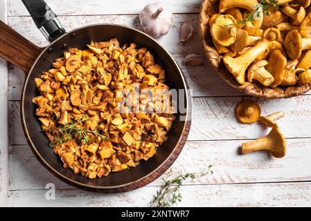 Funghi canterelle fritti in padella su sfondo di legno bianco, vista dall'alto, spazio per fotocopie. Funghi della foresta, galline crude e arrostite, cucina locale di stagione Foto Stock