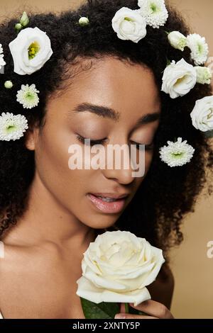 Una bella donna afroamericana con trucco naturale e fiori bianchi nei capelli, con una rosa bianca. Foto Stock