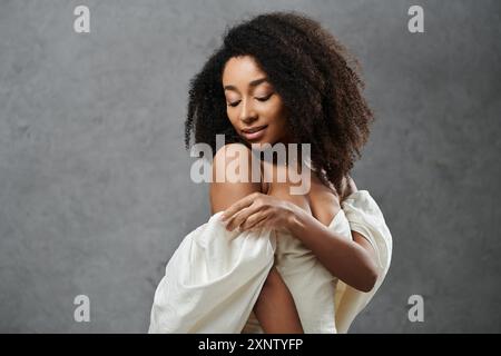 Una splendida sposa afroamericana in un abito da sposa bianco si posa su uno sfondo grigio Foto Stock