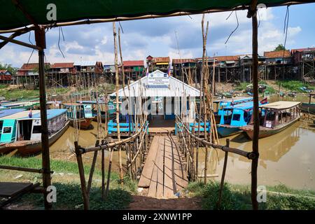 Barche in legno attraccate in un villaggio sul fiume Tonle SAP, con case a palafitte e passerelle in legno in una giornata di sole. Foto Stock