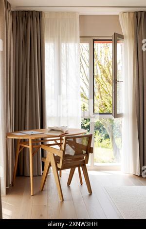 Scrivania in legno con poltrona in camera da letto. Finestre coperte da tende. Potete vedere il giardino fuori. Nessuno dentro. Foto Stock