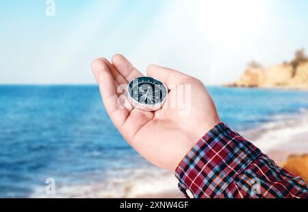 Uomo che tiene la bussola sulla spiaggia vicino al mare, primo piano Foto Stock