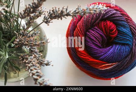 Palla in tessuto dai colori brillanti con bouquet di lavanda. Filato di lana colorato con lavanda in vaso. Ancora in vita. Hobby per lavorare a maglia. Lavorata a maglia. Foto Stock