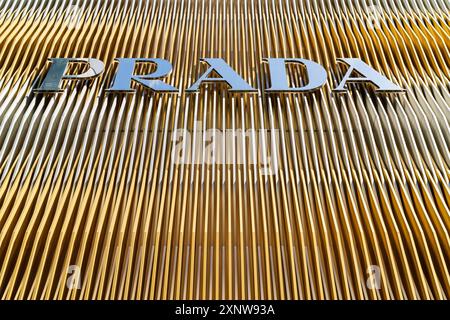 Il logo Prada e il nome del marchio torreggiano sullo spettatore sulla parte anteriore della facciata dorata delle spranghe metalliche del suo negozio Ginza a Tokyo. Foto Stock