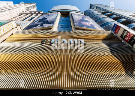 Il negozio Prada sulla Ginza. Vista ad angolo basso del logo Prada su spranghe in metallo dorato con due cartelloni giganti sopra. Foto Stock