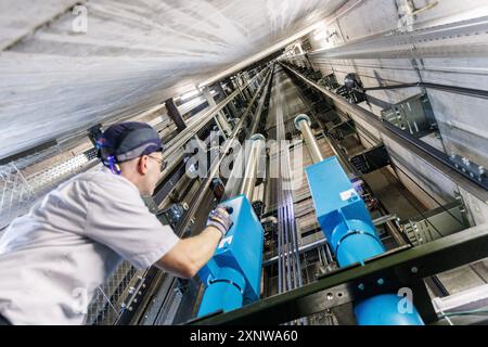 PRODUZIONE - 31 luglio 2024, Assia, Francoforte/M.: Markus Zink, tecnico di assistenza presso Schindler, ispeziona le funi metalliche nell'albero dell'elevatore alto 228,83 metri. Il produttore di ascensori Schindler testa vari componenti dei suoi ascensori nell'Europaturm, la torre televisiva di Francoforte. Foto: Lando Hass/dpa Credit: dpa Picture Alliance/Alamy Live News Foto Stock