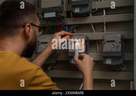 Uomo con candela che controlla il contatore elettrico in casa Foto Stock